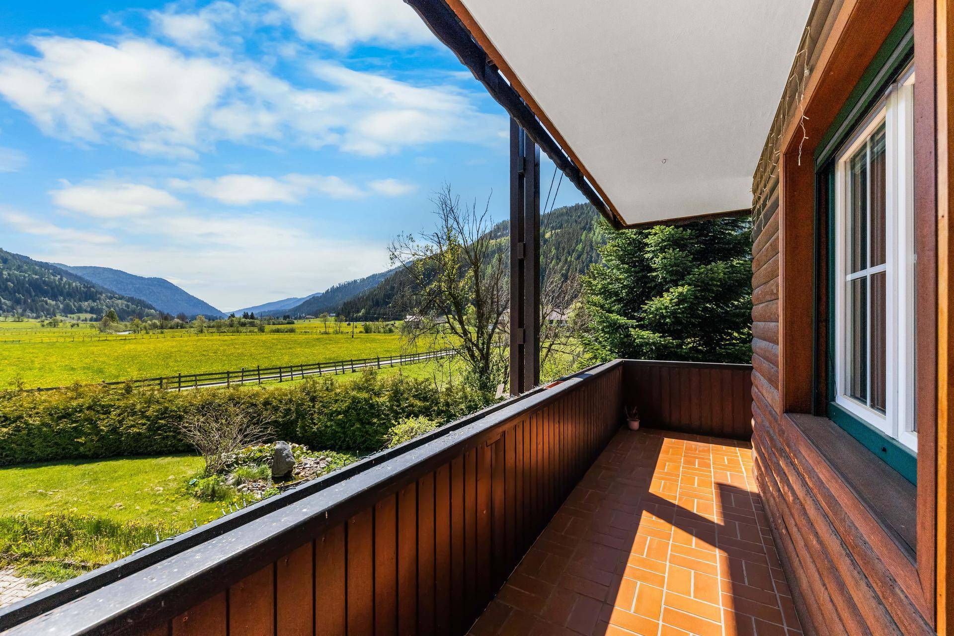 Geräumiger Balkon mit Terrakottafliesen und Holzverkleidung, bietet einen weiten Blick ins Tal.