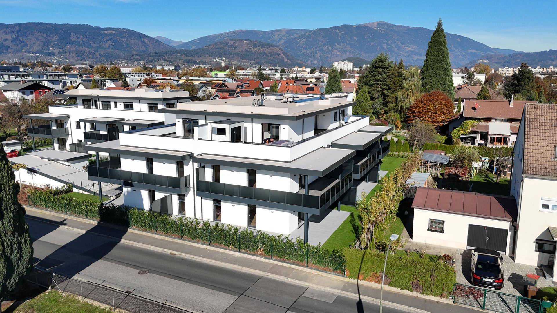 Moderne Wohngebäude mit Balkonen und Flachdach, eingebettet in eine grüne Landschaft mit Bergblick.