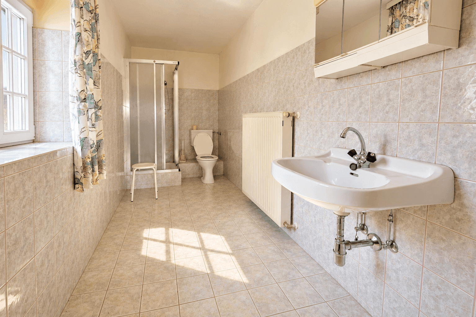 Funktionales Badezimmer mit hellen Fliesen, Dusche und Fenster, in gutem, aber älterem Zustand.