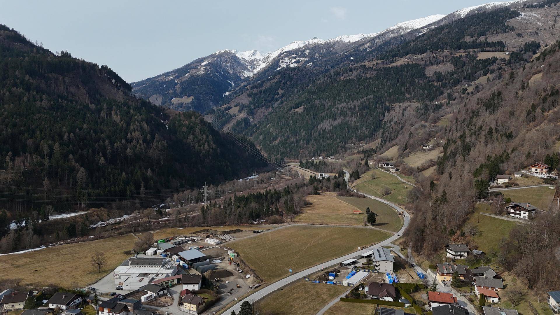 Panoramablick aus der Vogelperspektive auf ein weites Tal mit bewaldeten Hängen und schneebedeckten Gipfeln.
