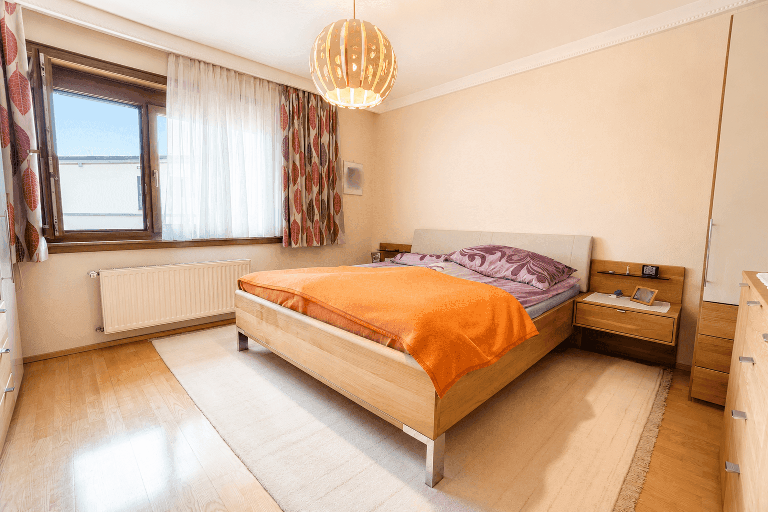 Helles Schlafzimmer mit Holzboden, modernem Bett und Fenster mit Blick ins Grüne.