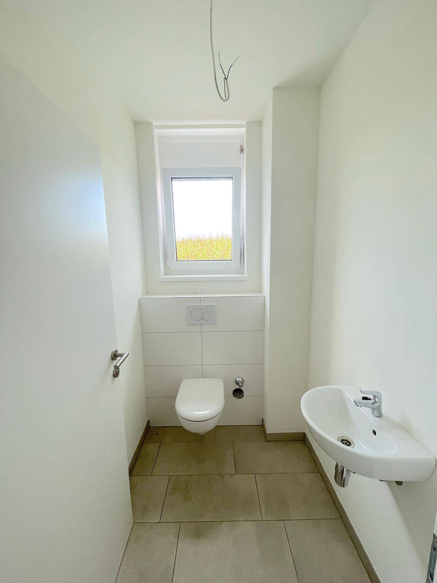 Separates Gäste-WC mit Fenster, wandhängender Toilette und kleinem Waschbecken.