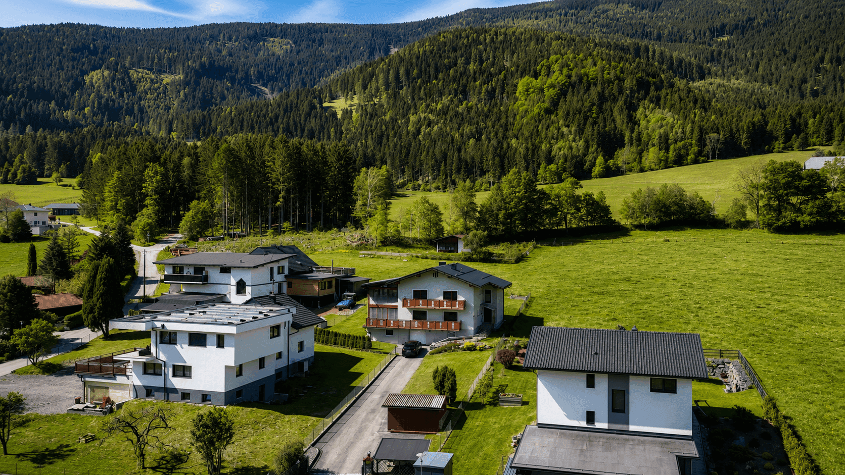 Luftaufnahme einer Wohnsiedlung mit mehreren Häusern und weitläufigen Grünflächen.