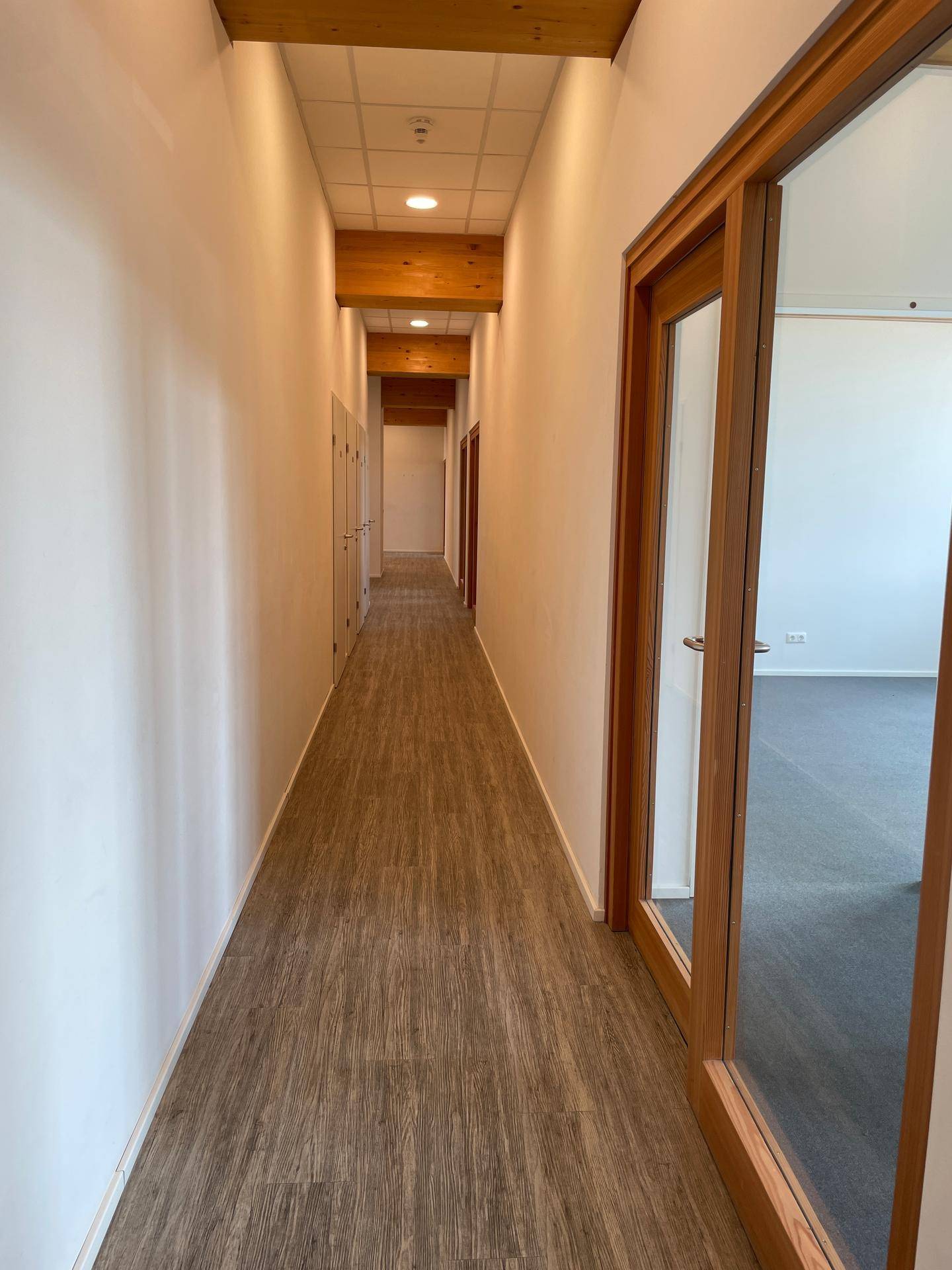 Langer Flur mit mehreren Türen, Holzbalken an der Decke und hellem Bodenbelag.