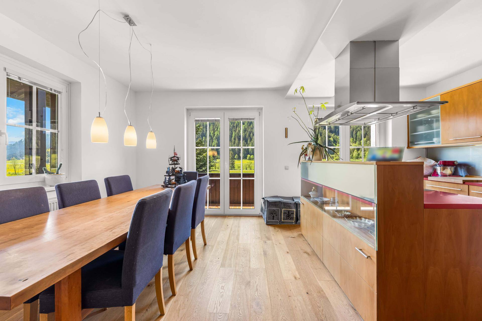 Heller Wohn-Essbereich mit Holzboden, moderner Küche und Zugang zu einem Balkon mit Bergblick.
