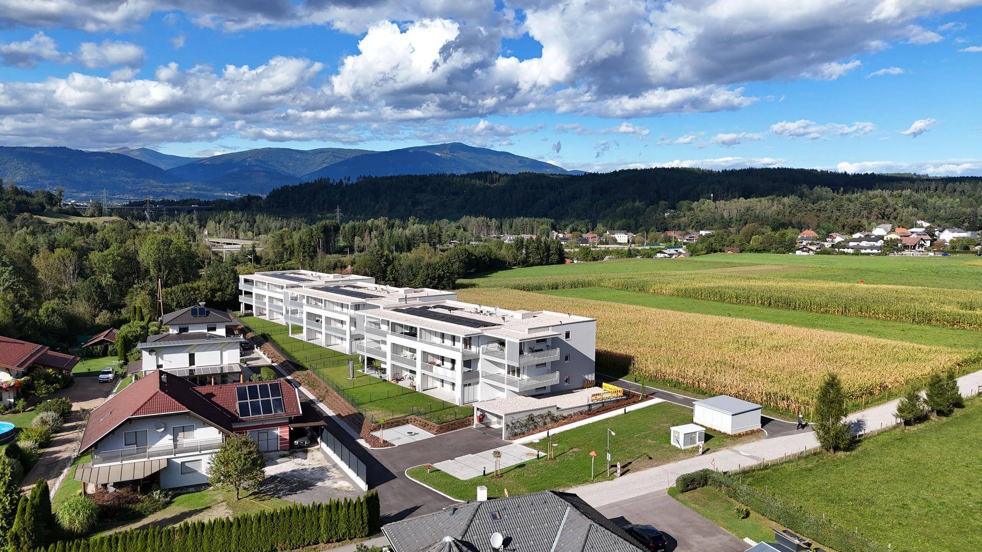 Weitläufige Luftaufnahme der Wohnanlage, umgeben von Feldern und Wäldern mit Bergsicht.