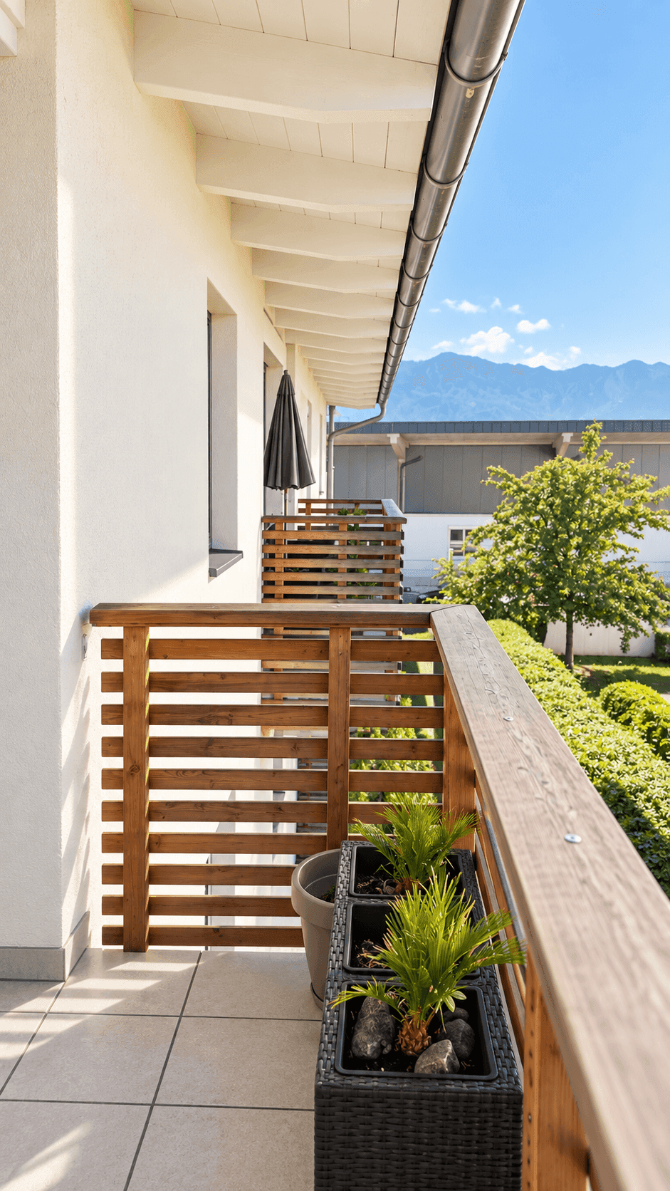 Langer Balkon mit Holzelementen, Pflanzen und einem weiten Blick auf die Berge.