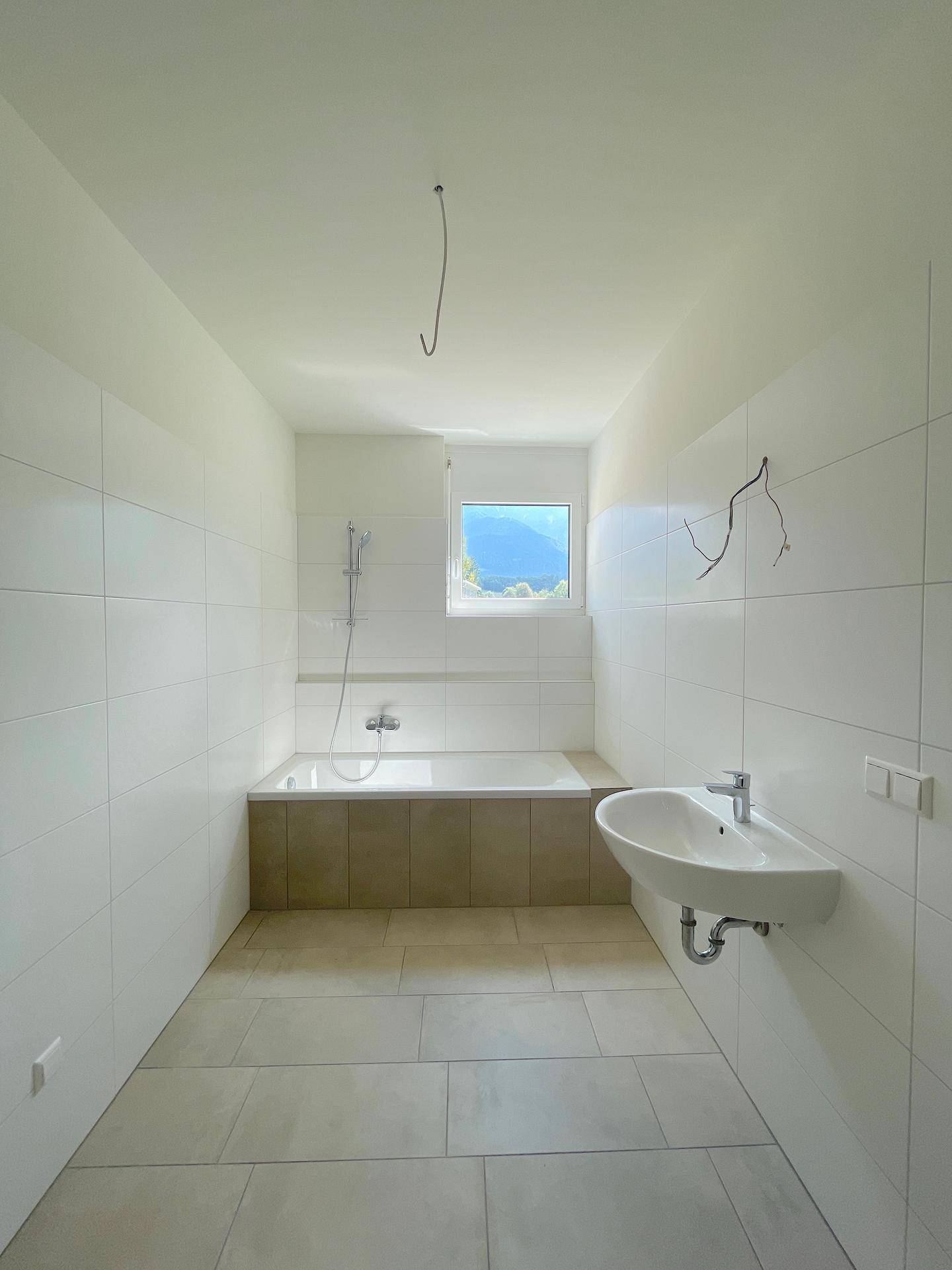 Modernes Badezimmer mit Badewanne, Waschbecken und Fenster, hell gefliest.