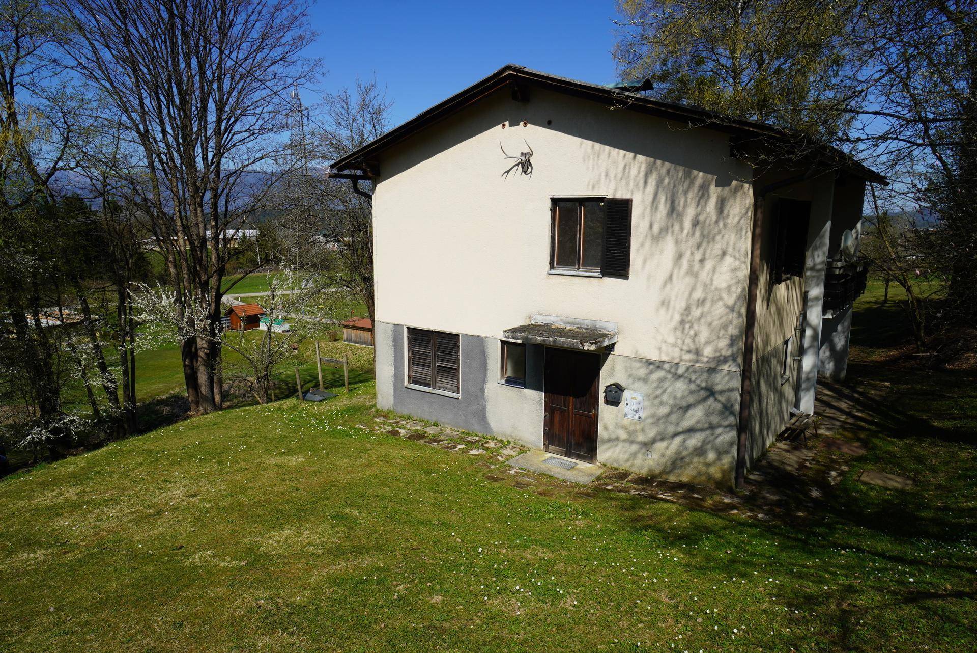 Einfamilienhaus mit heller Fassade und dunklen Fensterläden, umgeben von einem gepflegten Rasen und Bäumen.