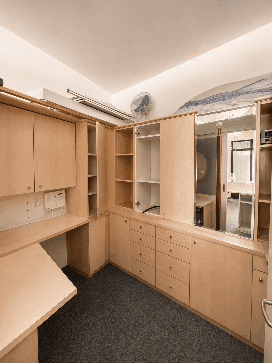 Funktionaler Büroraum mit maßgefertigten Holzschränken, integriertem Schreibtisch und einem Deckenventilator.