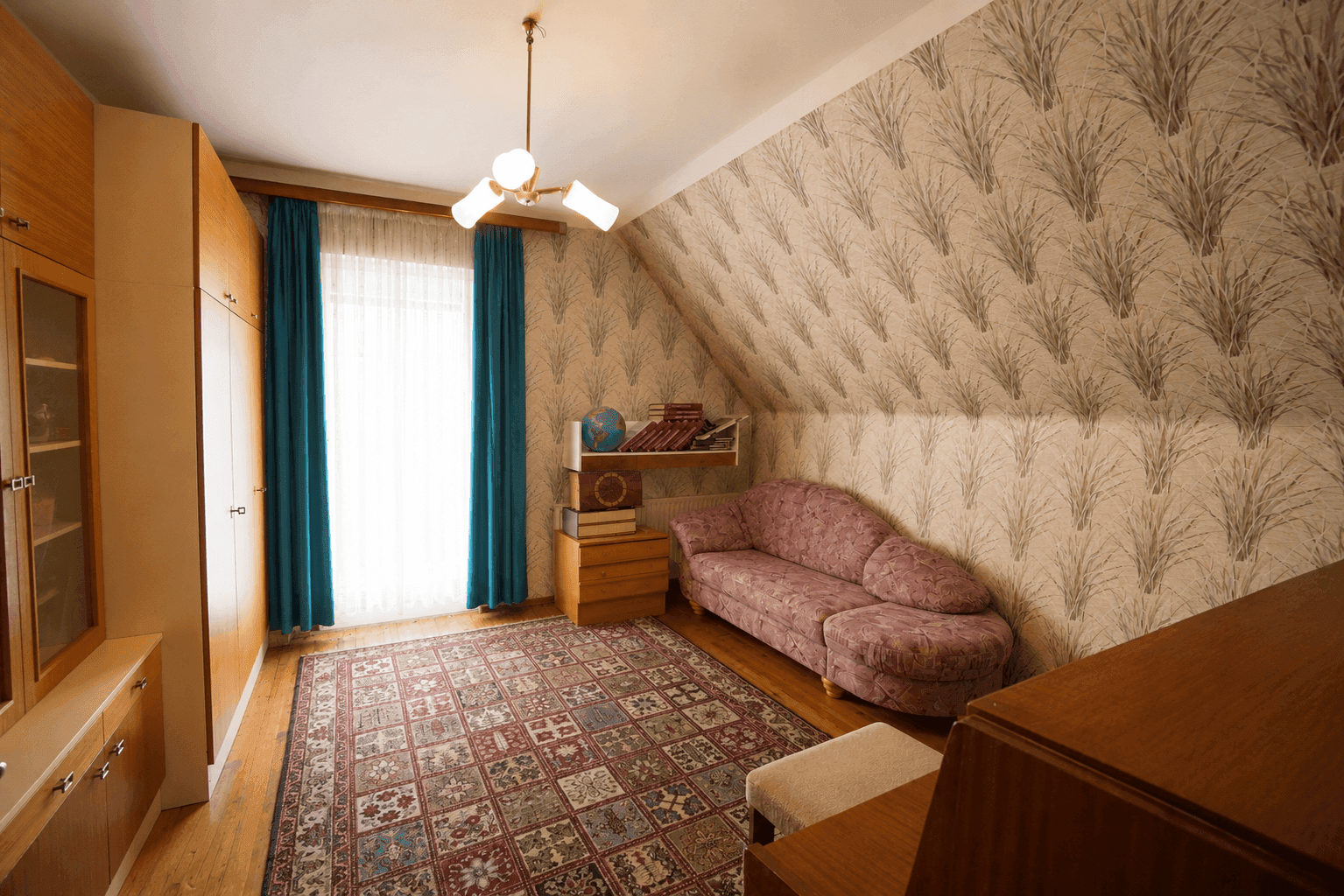 Dachzimmer mit Sofa, Schränken, gemusterter Tapete und Holzdielenboden, ideal als Gästezimmer.