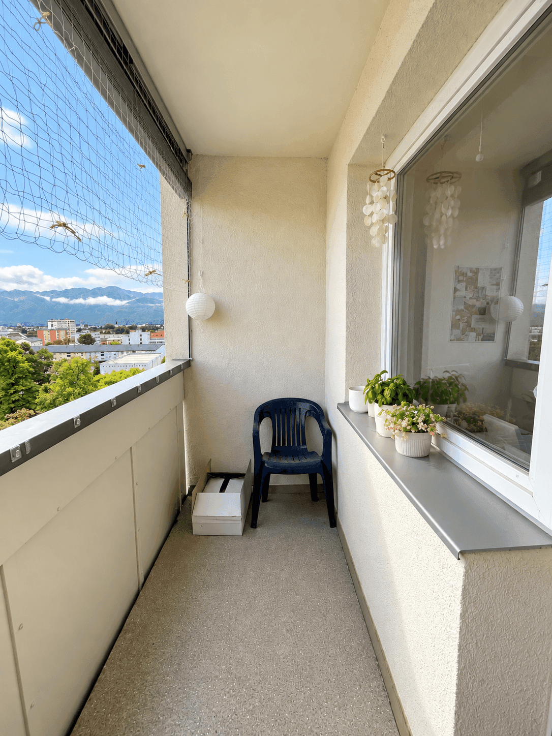 Kleiner Balkon mit Stadt- und Bergblick, ausgestattet mit einem einfachen Stuhl und Pflanzen.