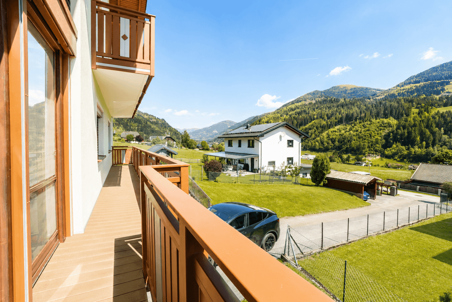Sonniger Balkon mit Holzboden und Geländer, bietet einen weiten Blick auf die Berge.