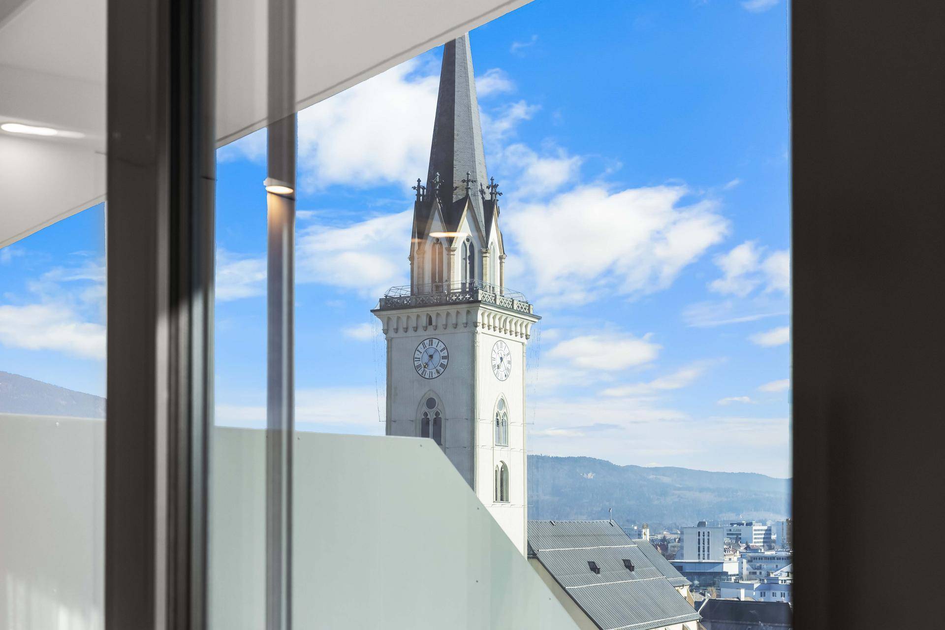 Blick aus dem Fenster auf einen historischen Kirchturm und die umliegende Stadtlandschaft.