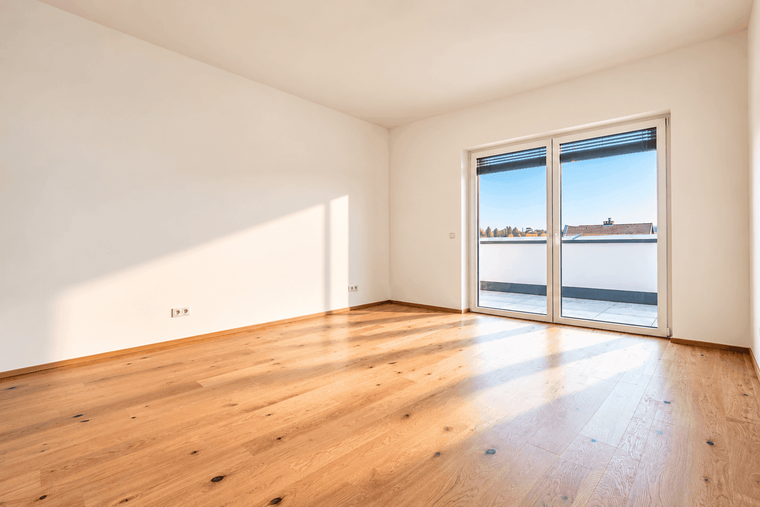 Leeres Schlafzimmer mit Holzboden und Zugang zu einem Balkon oder einer Terrasse.