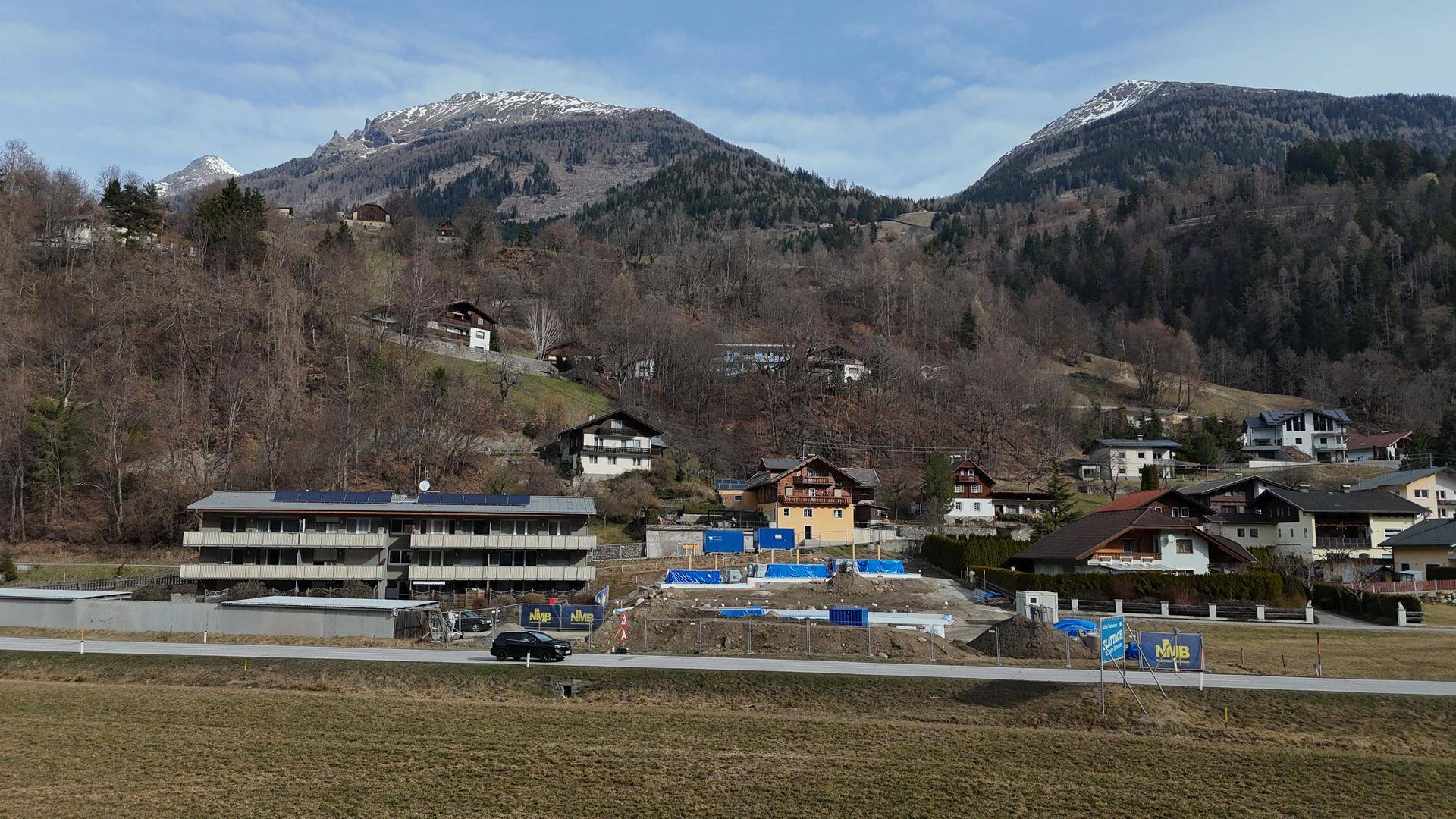 Blick auf eine ländliche Ortschaft mit Bergen im Hintergrund und einer Baustelle im Vordergrund.