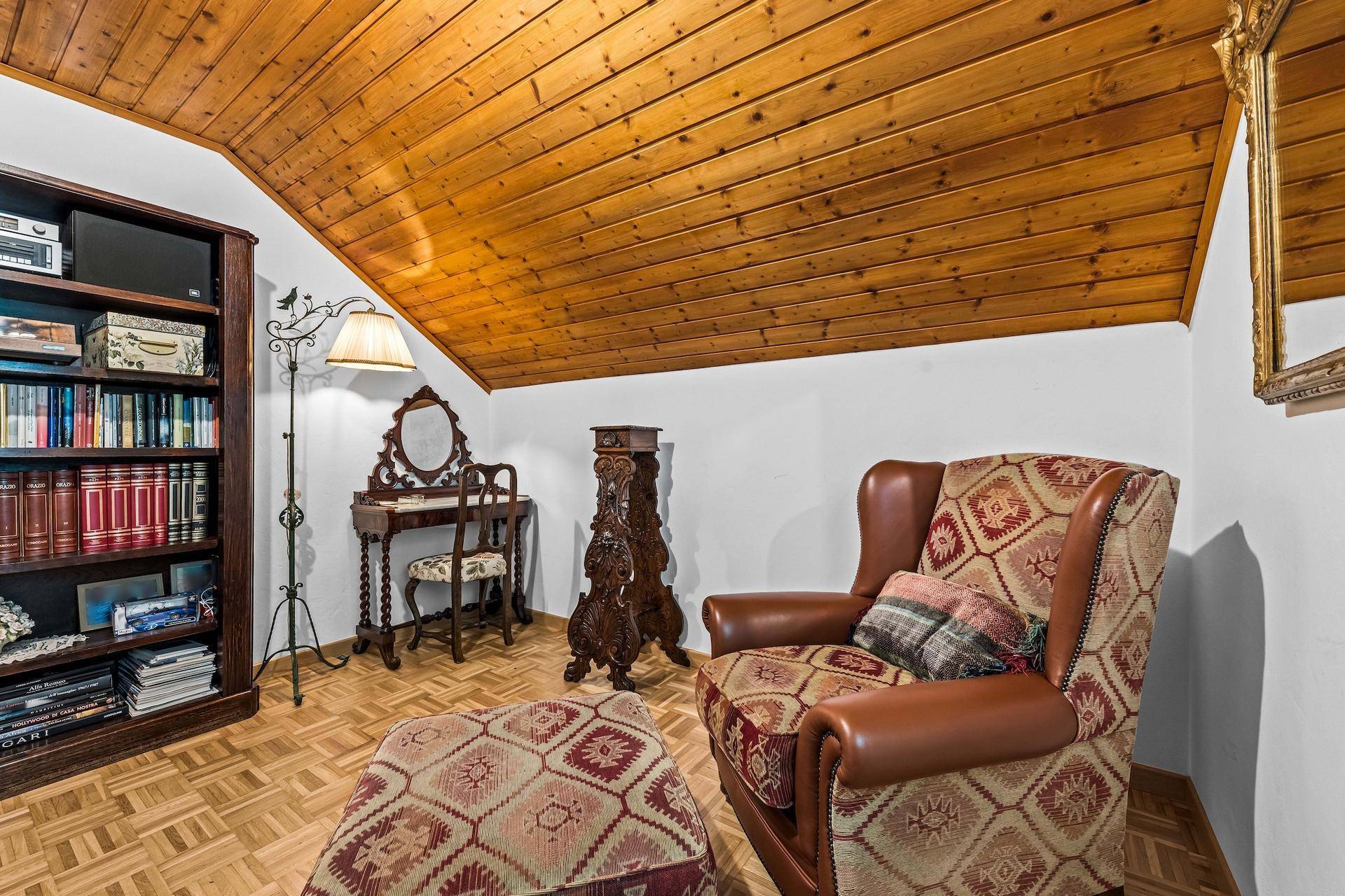 Gemütlicher Lesebereich mit Sessel, Bücherregal und Holzboden unter einer Dachschräge.