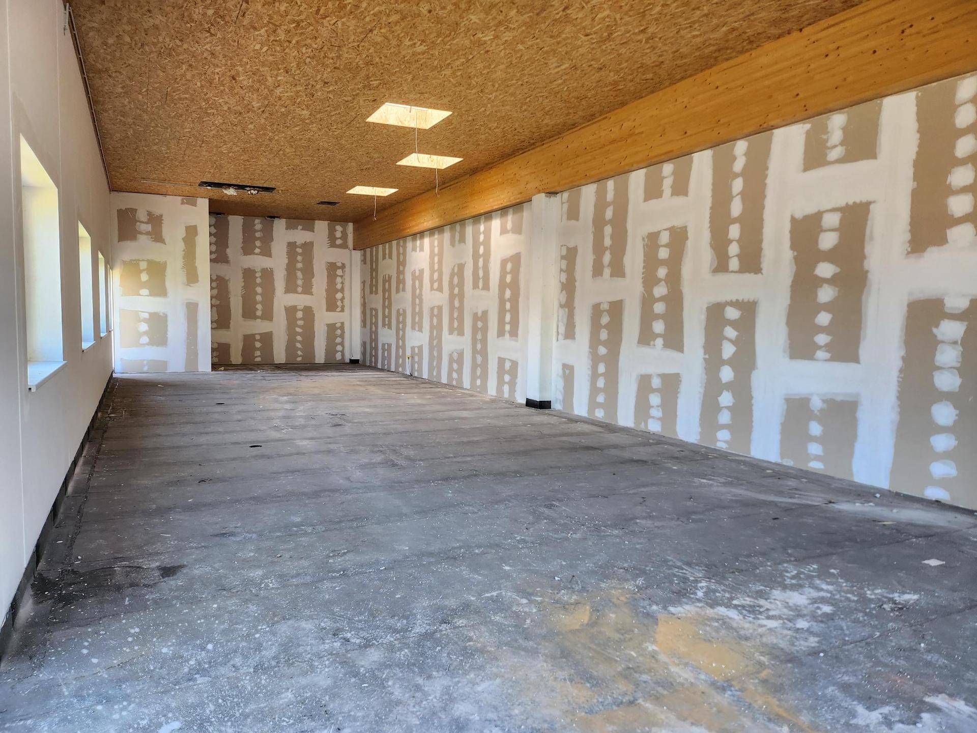 Geräumiger, unmöblierter Geschäftsraum mit OSB-Decke und vorbereiteten Wänden für den Innenausbau.