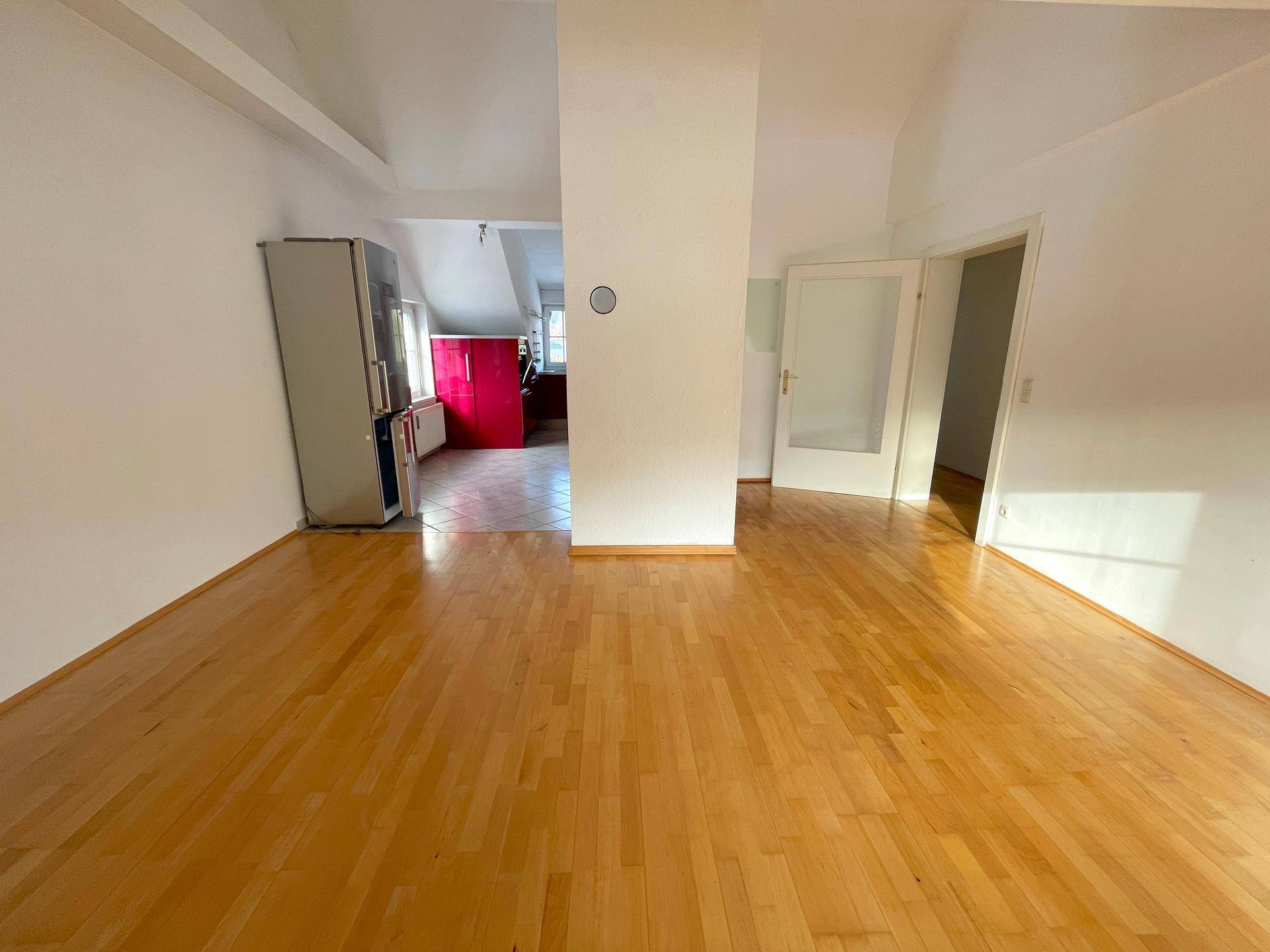 Offener Wohnbereich mit Holzboden, der in eine moderne Küche mit roten Schränken übergeht.
