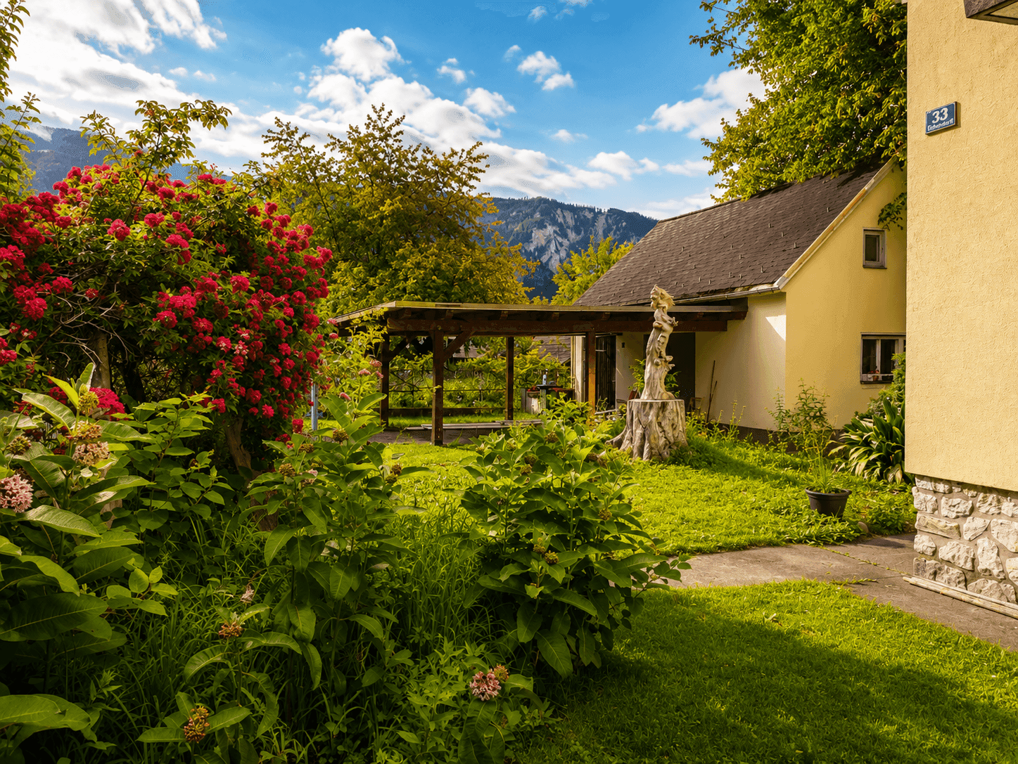 Gepflegter Gartenbereich neben dem Haus mit Rasenfläche, Sträuchern und einer überdachten Terrasse.