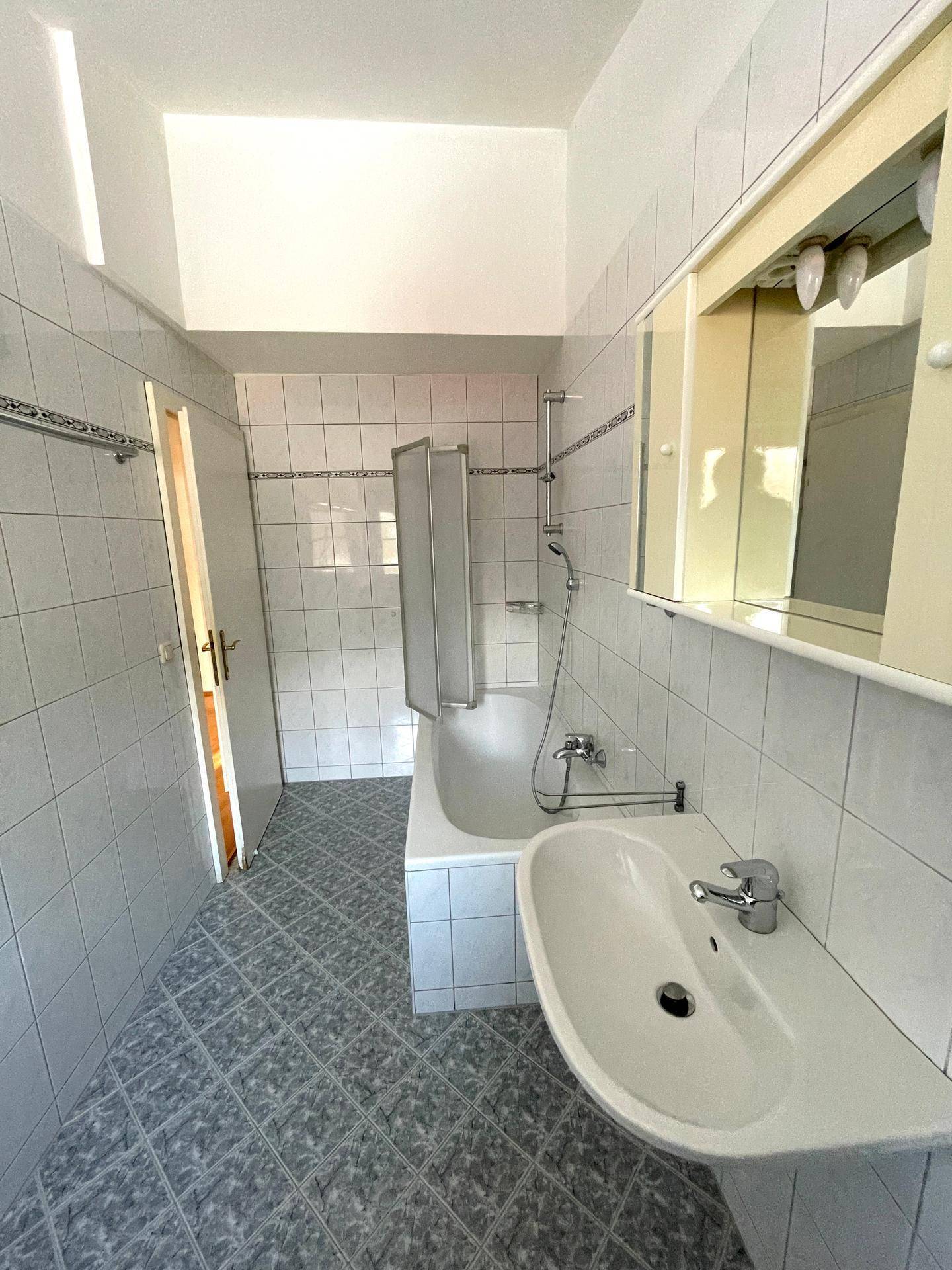 Funktionales Badezimmer mit Badewanne, Duschvorhang, Waschbecken und großem Spiegelschrank.