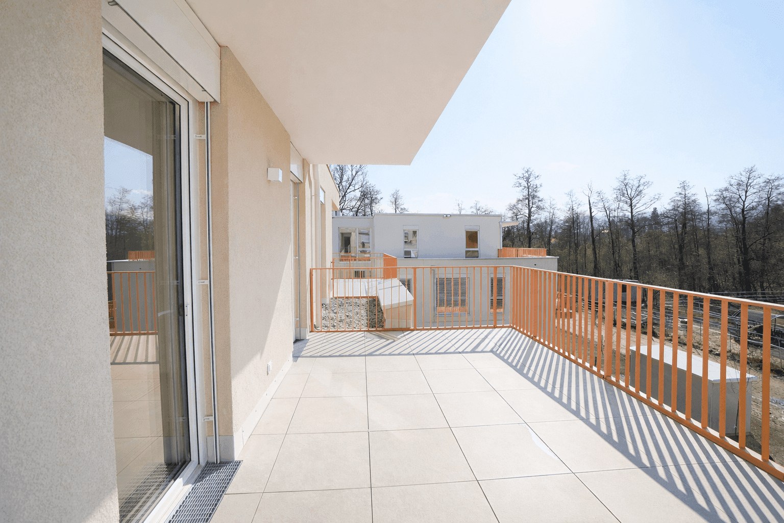 Große, sonnige Terrasse mit Fliesenboden und Blick auf die umliegenden Gebäude.