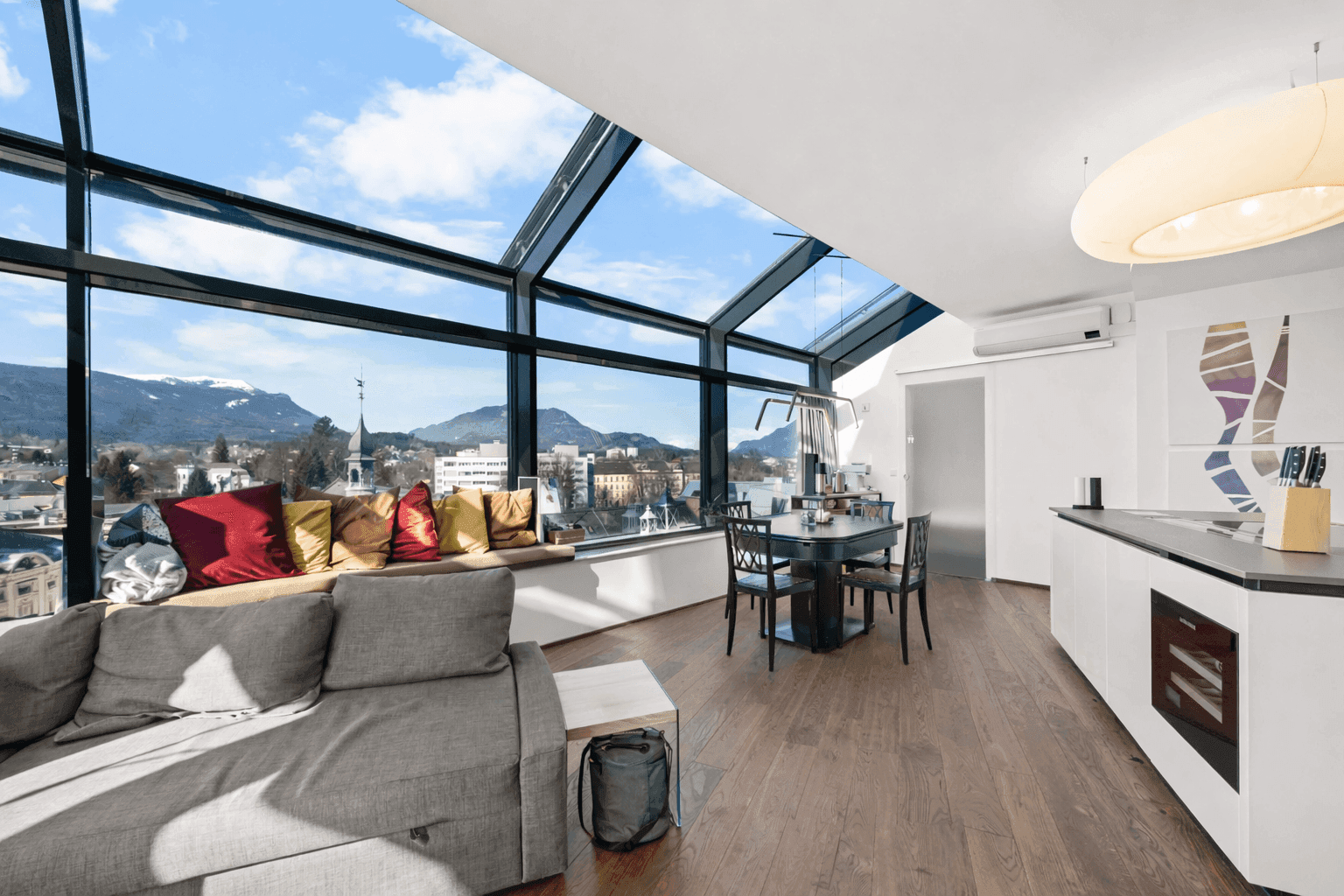 Heller Wohn- und Essbereich mit großen Glasfronten, Holzboden und atemberaubendem Stadt- und Bergblick.