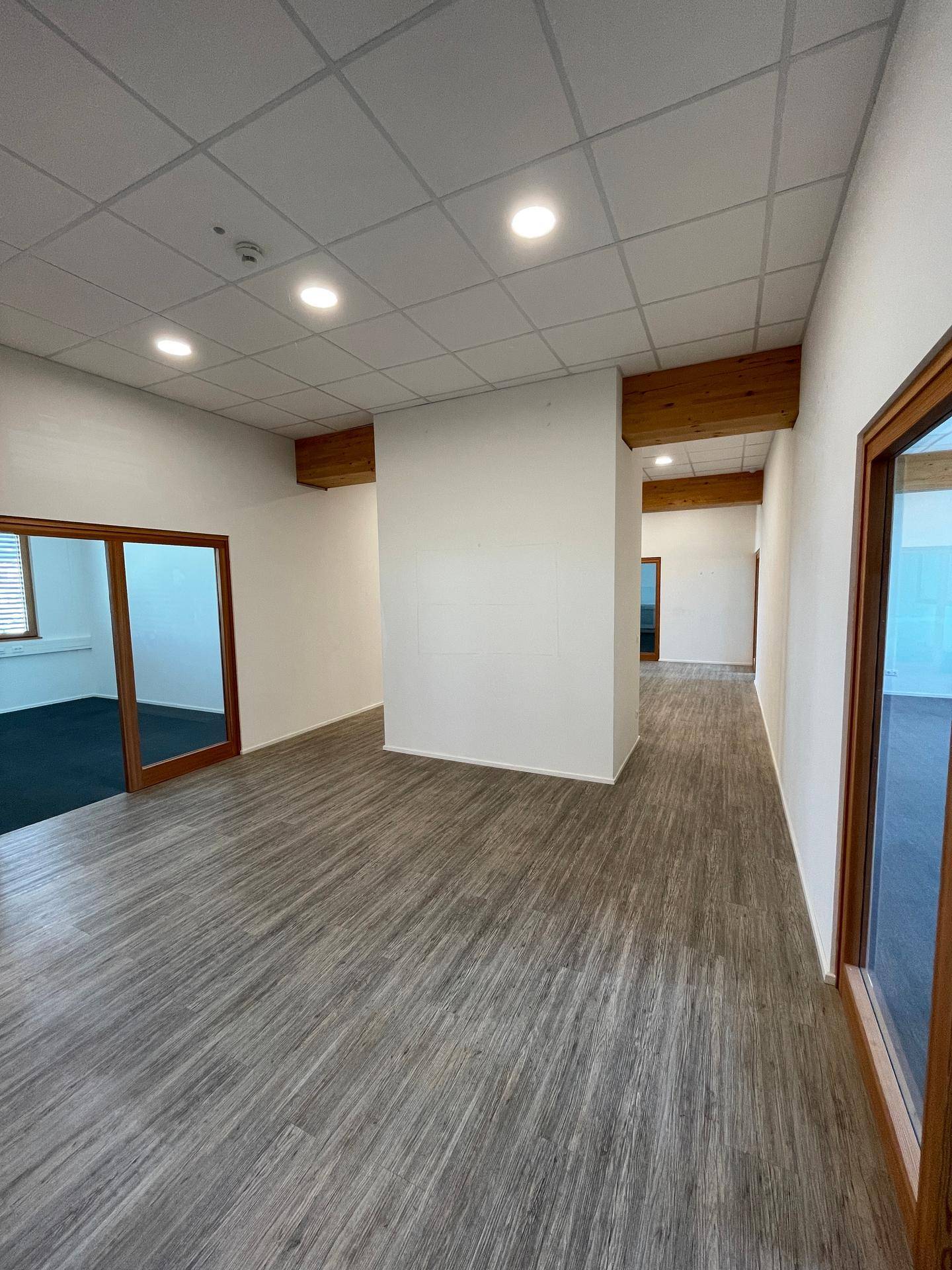 Großer, offener Bürobereich mit hellem Boden, weißen Wänden und sichtbaren Holzbalken.