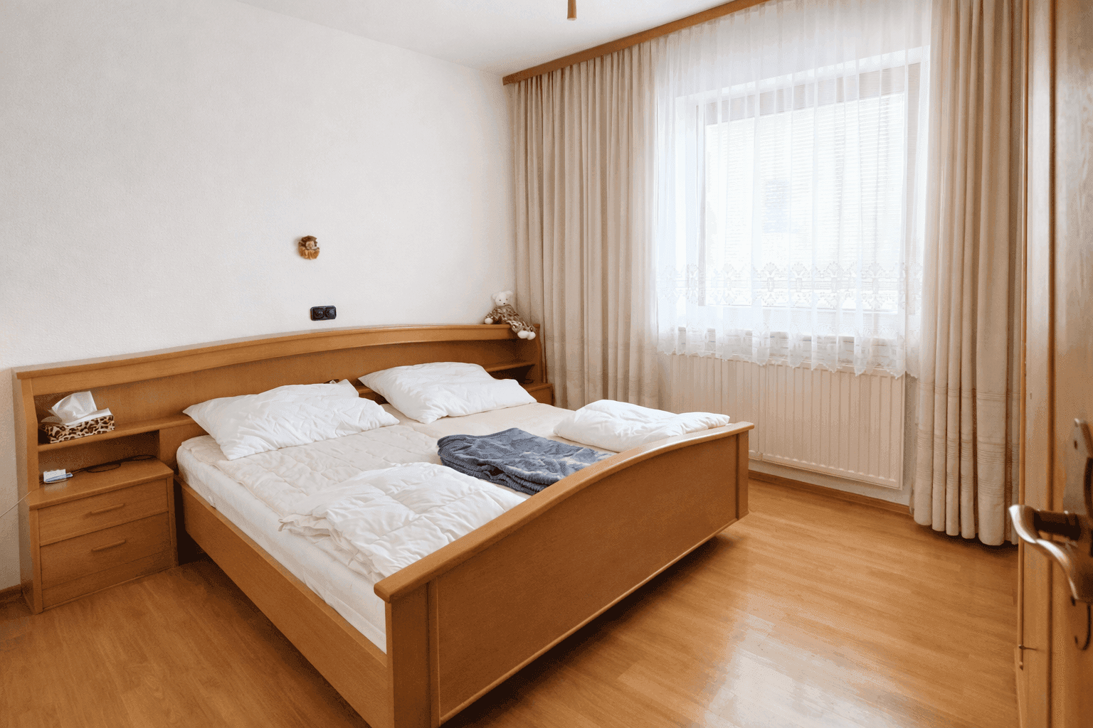 Helles Schlafzimmer mit Doppelbett, Holzmöbeln und Parkettboden.