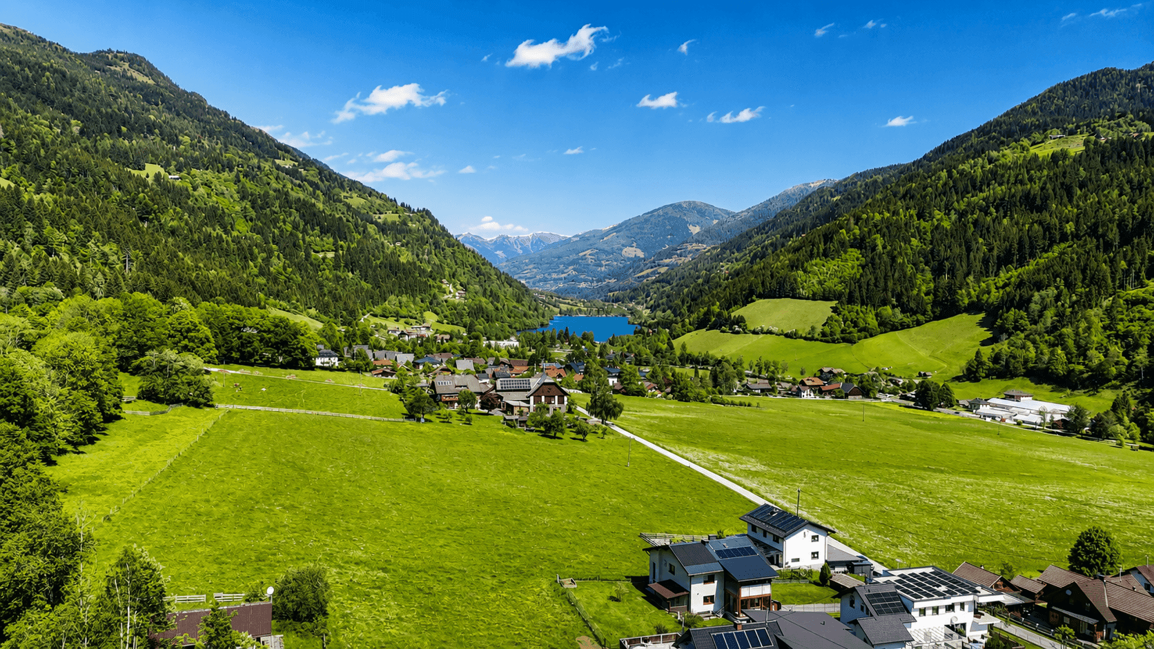 Weitläufige Landschaft mit einem See, umgeben von grünen Bergen und kleinen Siedlungen.