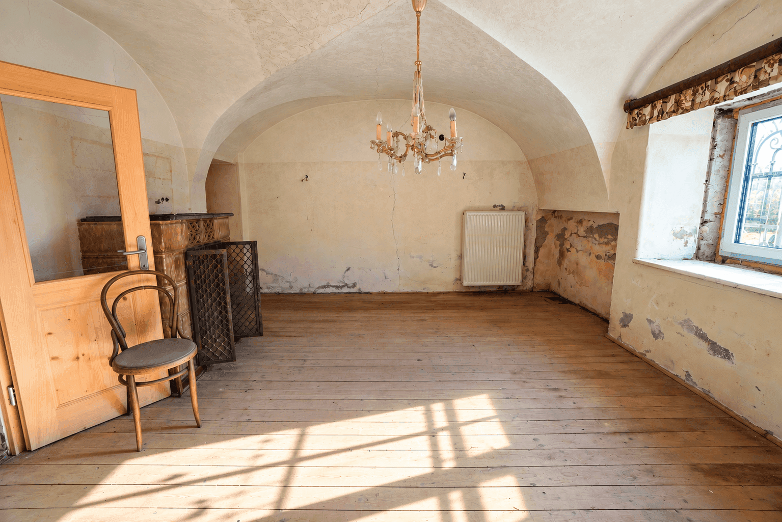 Leerer Raum mit Holzdielenboden, Gewölbedecke und Renovierungsbedarf, beleuchtet von Sonnenlicht.