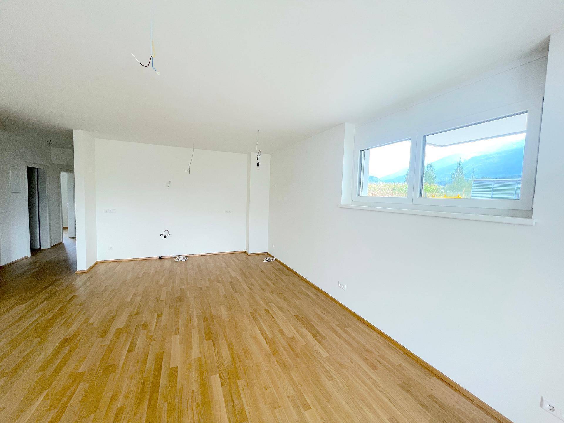 Geräumiges Wohnzimmer mit hellem Holzboden und großen Fenstern, bereit für die Einrichtung.