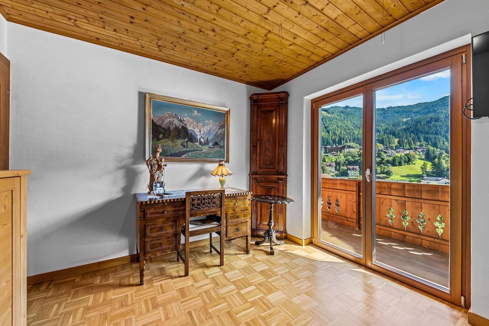 Helles Zimmer mit Holzboden, Schreibtisch und Balkonzugang mit Bergblick.