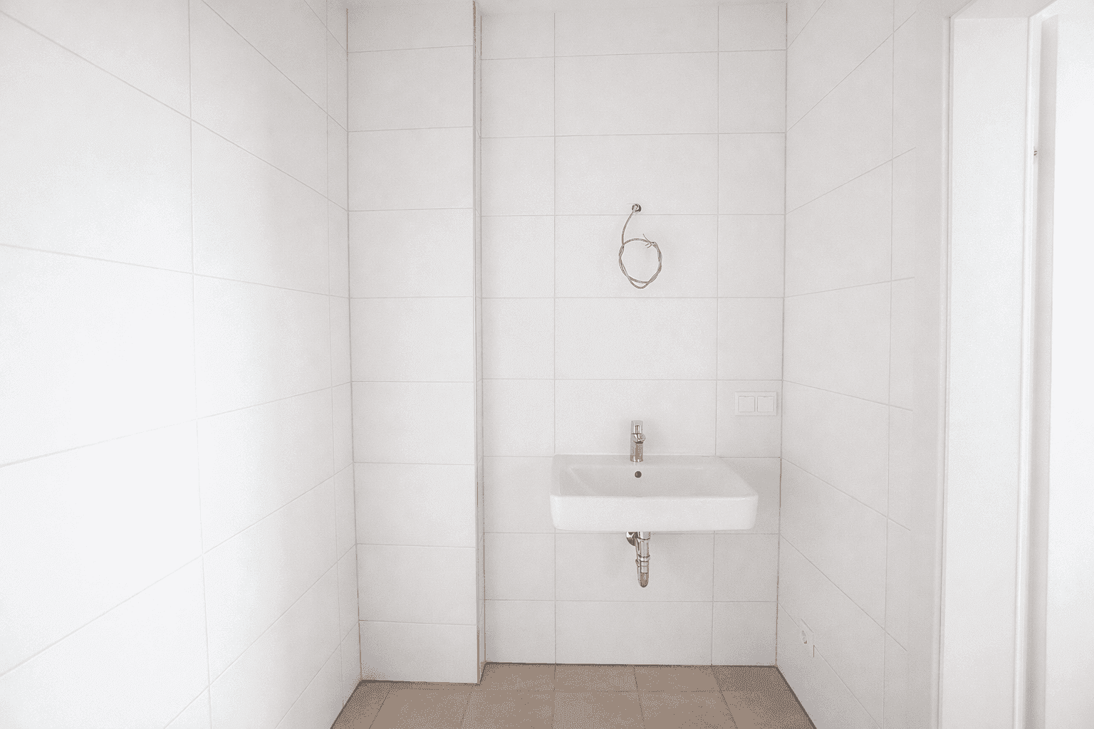 Helles Badezimmer mit weißen Wandfliesen und einem einzelnen Waschbecken in minimalistischem Design.