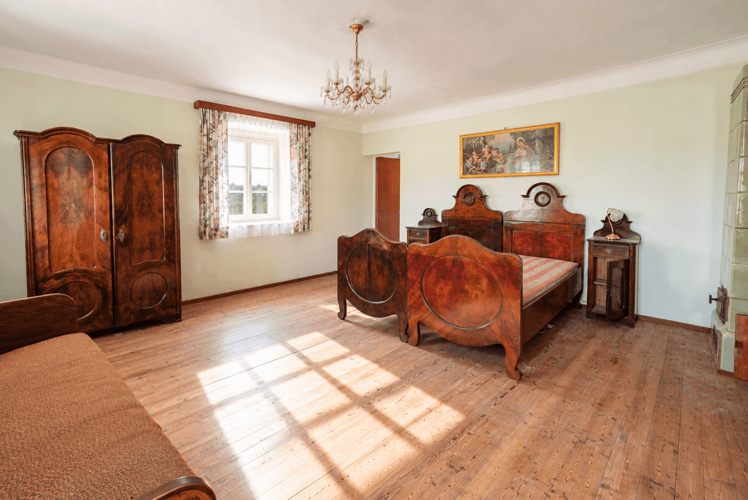 Großes Schlafzimmer mit Holzdielenboden und Kachelofen, ausgestattet mit antiken Holzmöbeln.