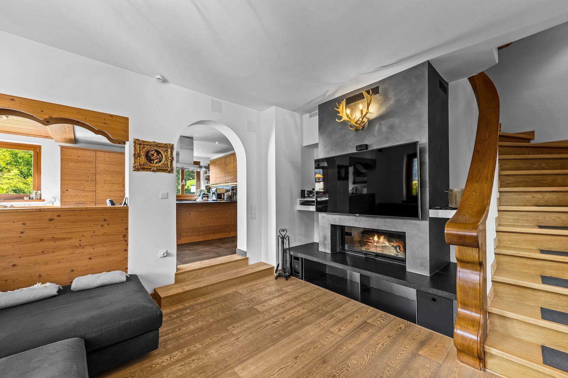 Gemütliches Wohnzimmer mit Kamin, Fernseher und Holztreppe, die in die obere Etage führt.