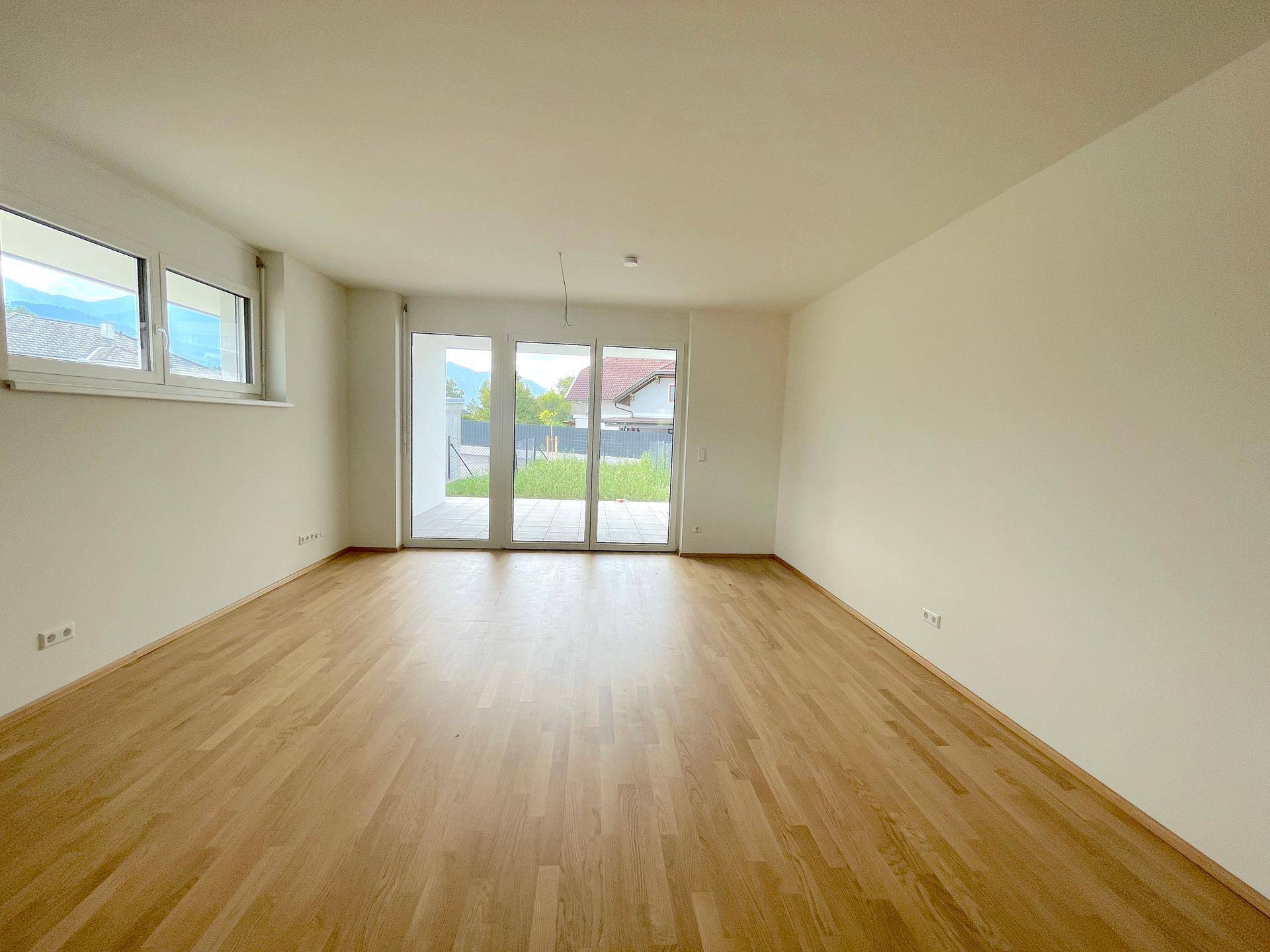 Helles Wohnzimmer mit Holzboden und Zugang zur Terrasse, umgeben von grüner Landschaft.