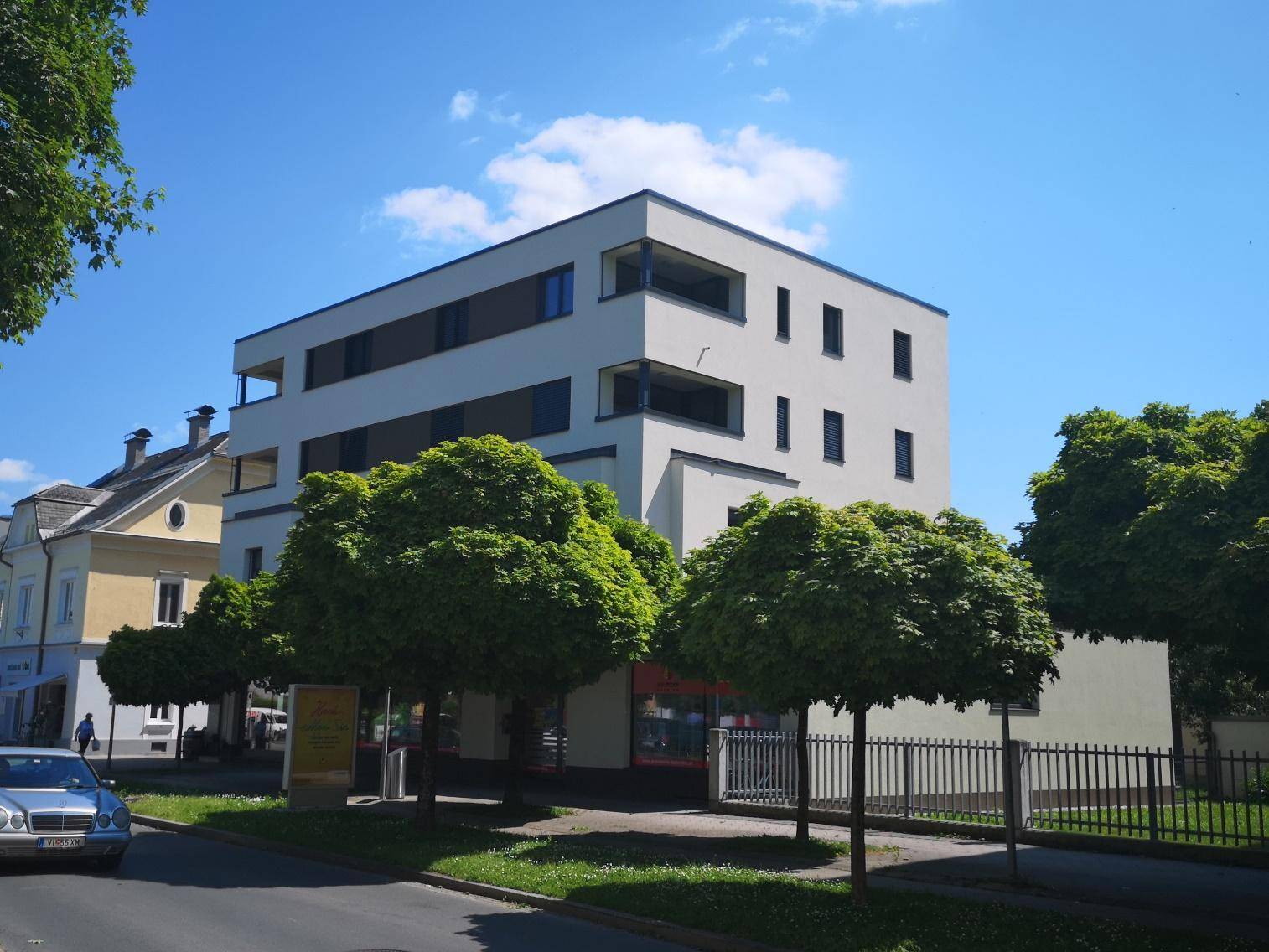 Modernes Mehrfamilienhaus mit klarer Architektur und Flachdach an einer begrünten Straße.
