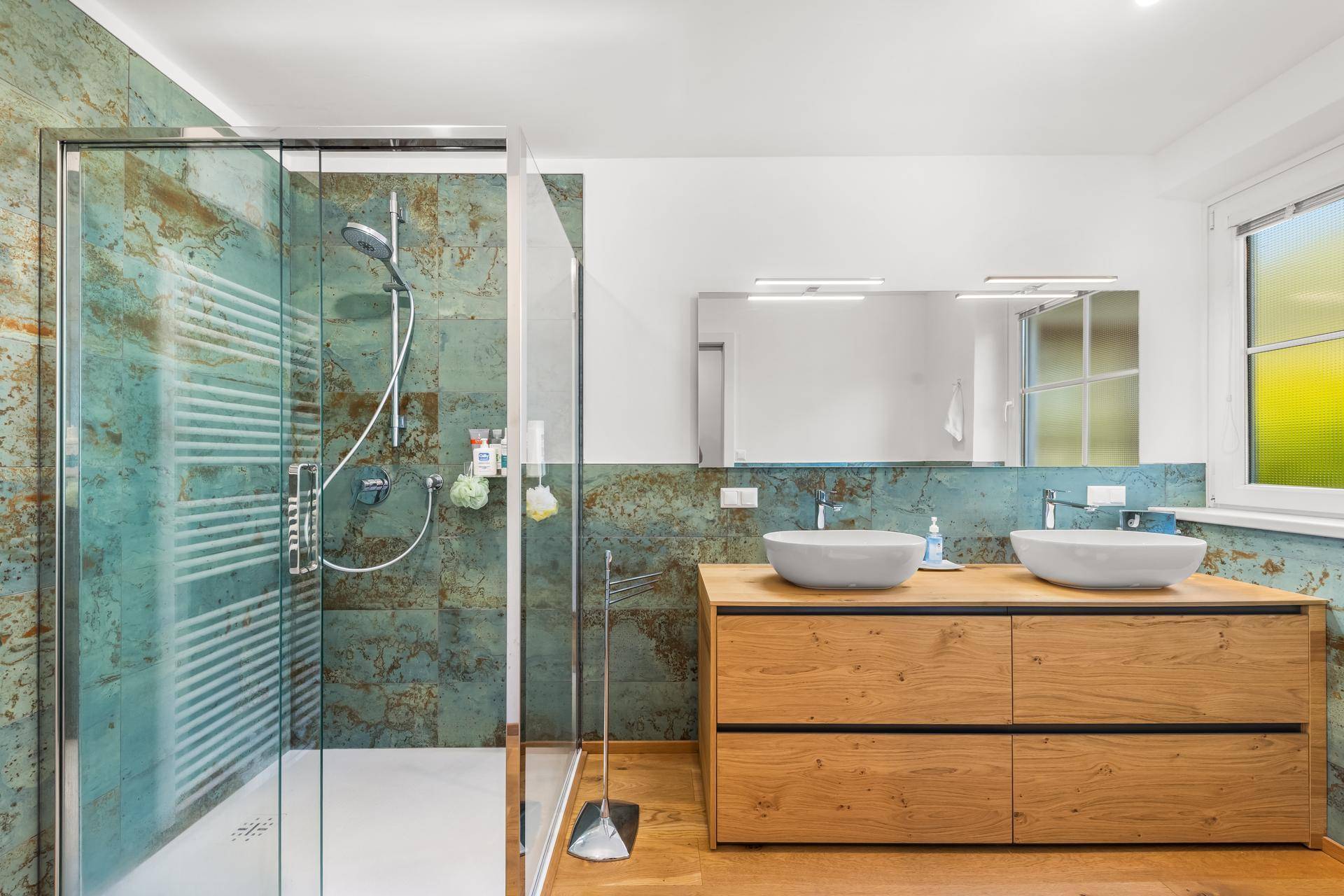 Modernes Badezimmer mit großer begehbarer Dusche, Doppelwaschbecken und auffälligen grünen Fliesen.