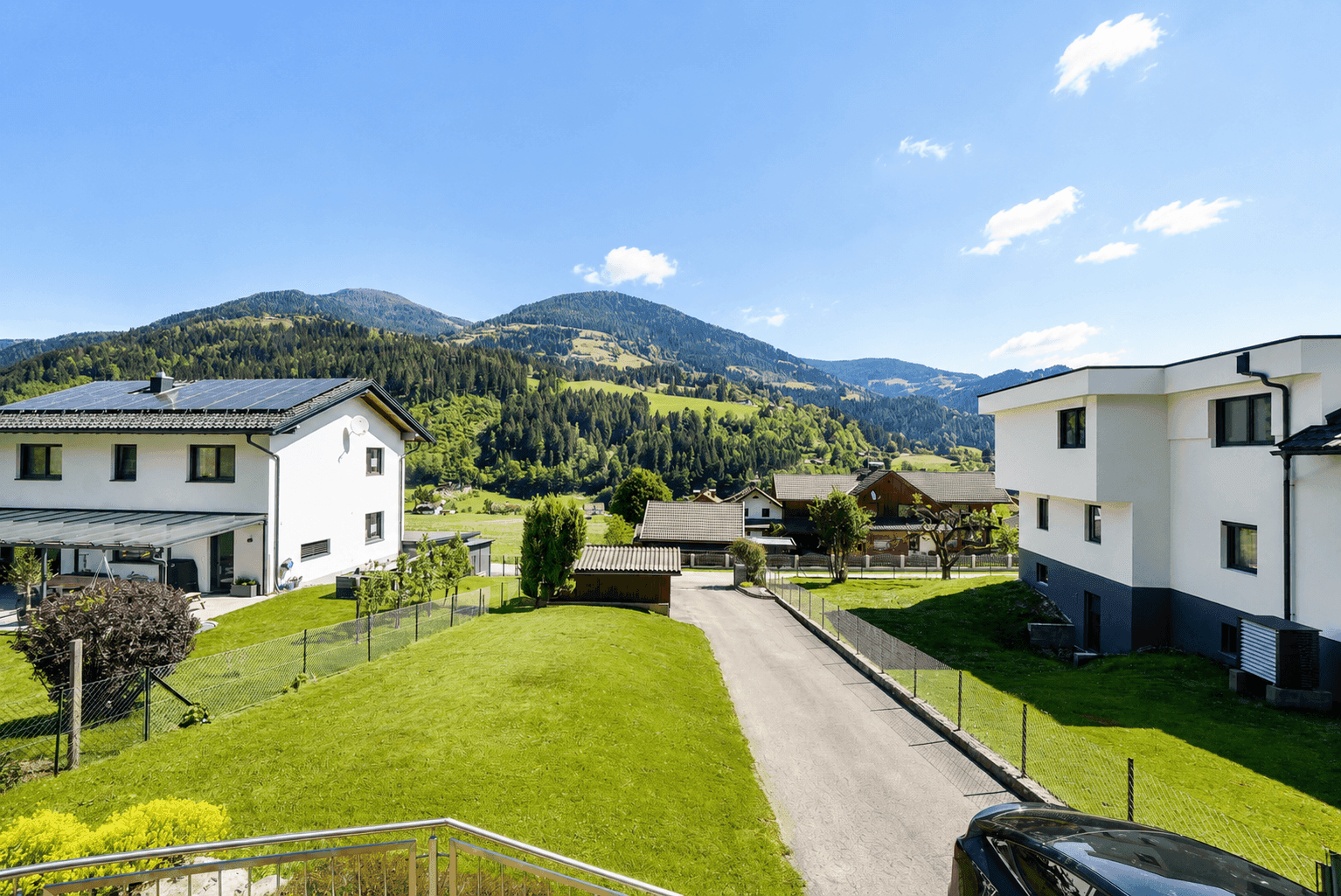 Blick auf die Nachbarschaft mit modernen Häusern und grünen Gärten vor Bergkulisse.