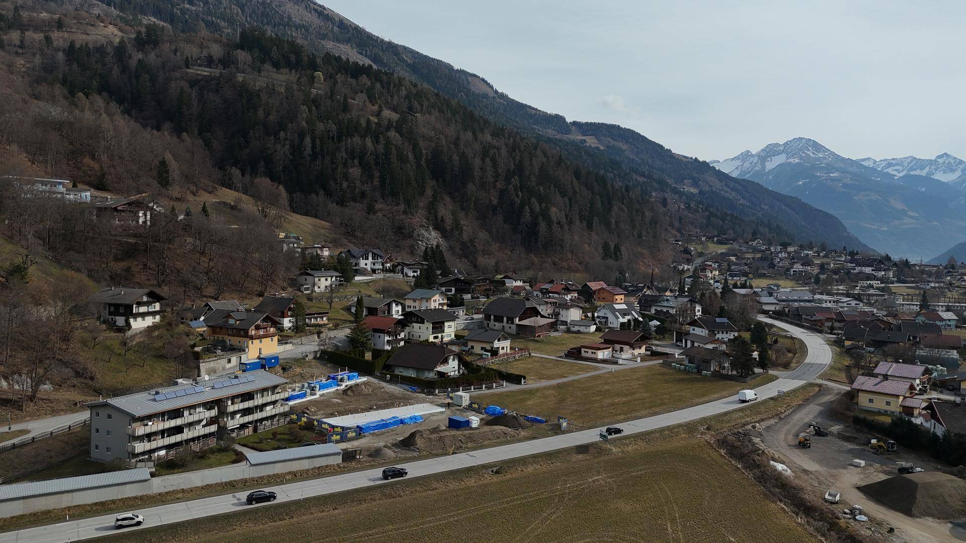 Weitläufige Luftaufnahme eines Tals mit Siedlungen, Straßen und schneebedeckten Bergen.