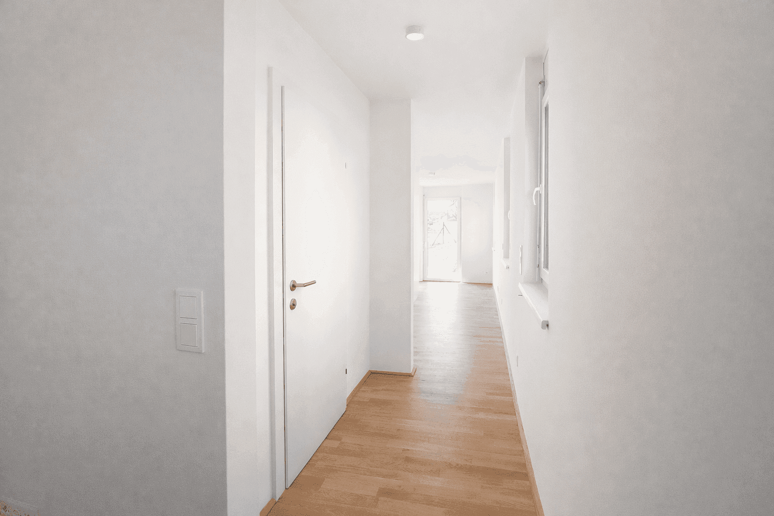 Heller Eingangsbereich mit Holzboden, weißen Wänden und einer modernen Tür.