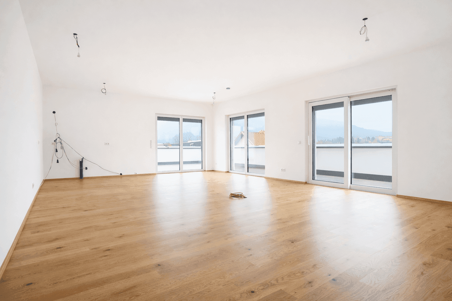 Heller, leerer Wohnraum mit Eichenparkettboden und großen Schiebetüren zur Terrasse.