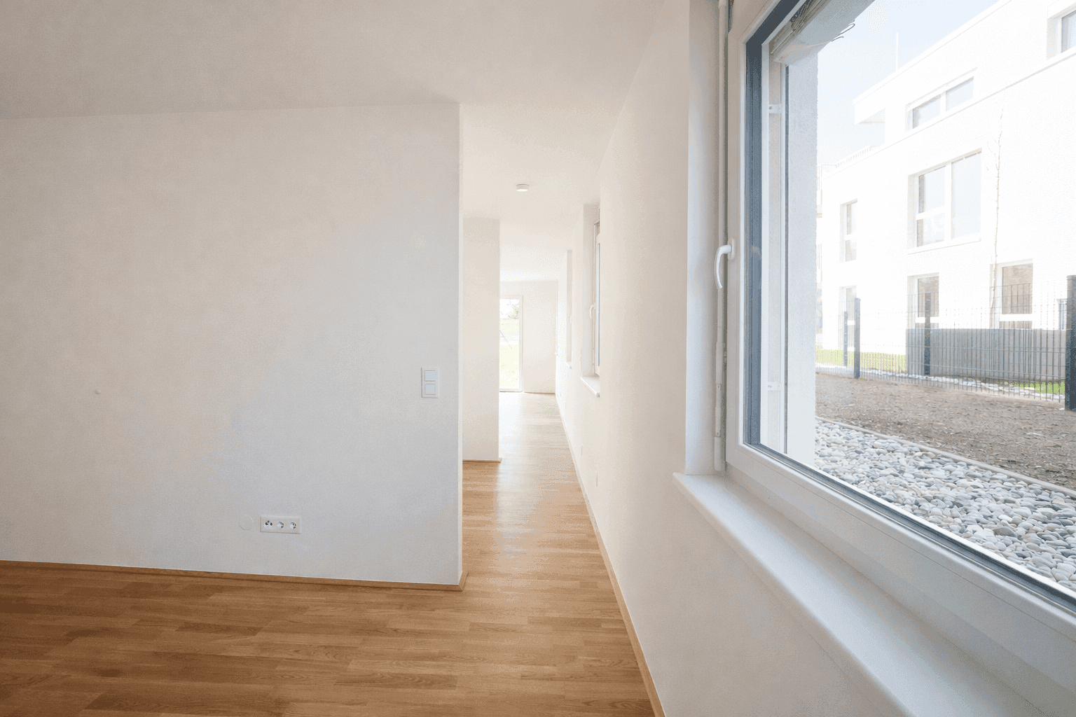 Langer, heller Flur mit Holzparkettboden und Fenstern, die den Blick nach draußen freigeben.