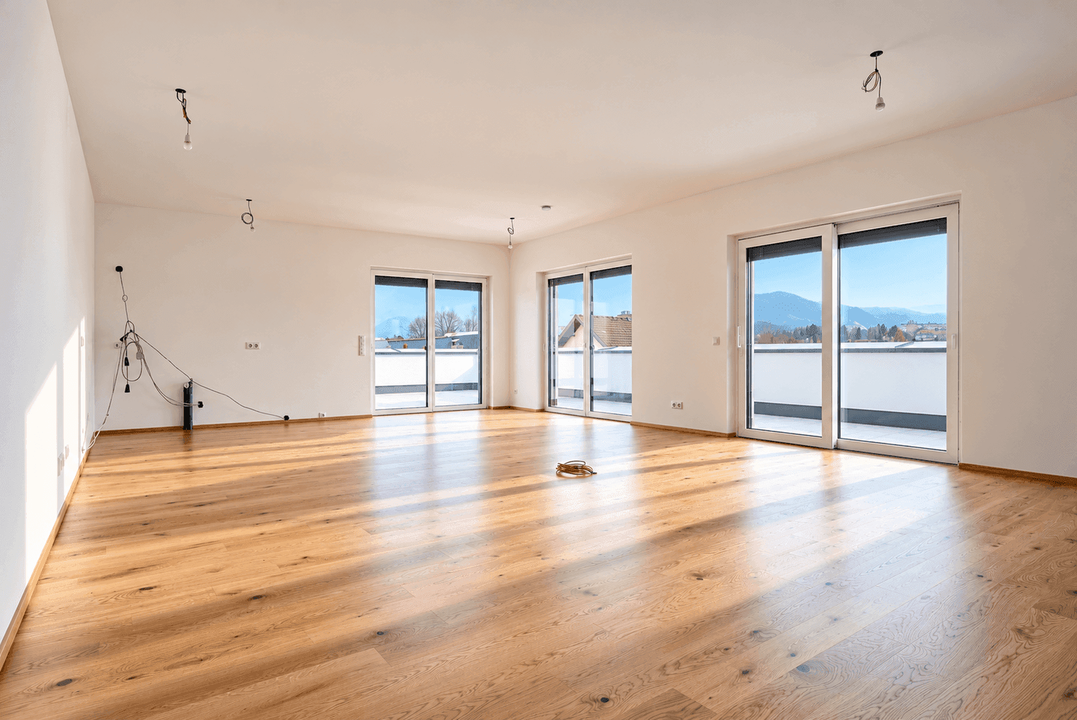 Großes, leeres Wohnzimmer mit Holzboden und mehreren Schiebetüren zur Terrasse.