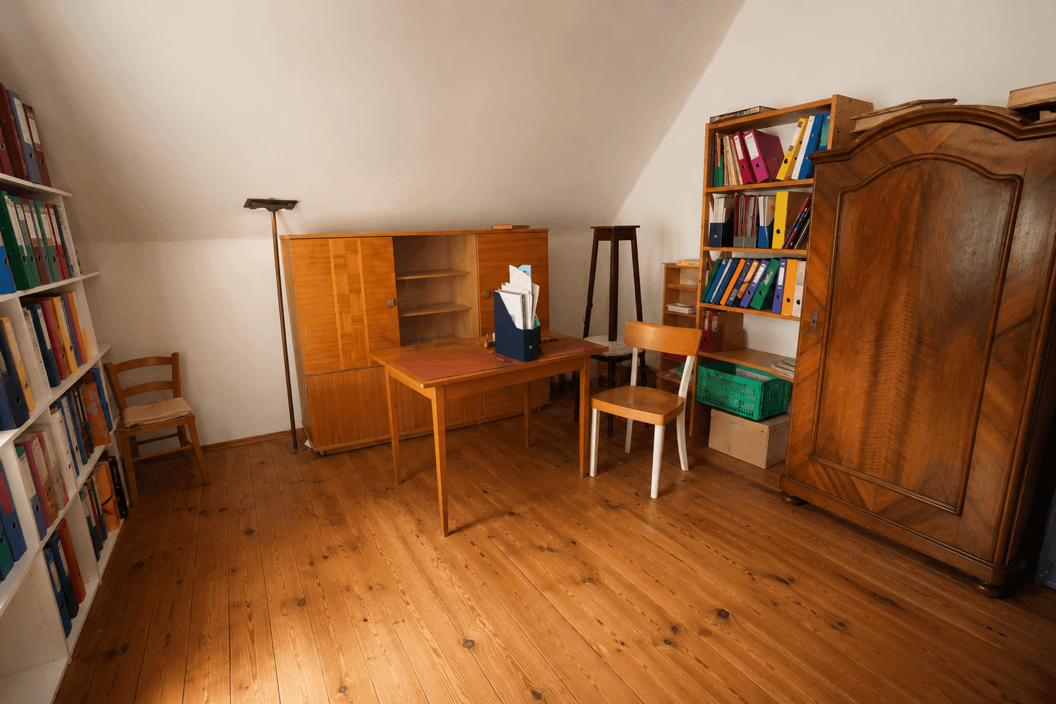 Helles Dachzimmer als Büro oder Arbeitsbereich mit Holzmöbeln, Regalen und Holzdielenboden.