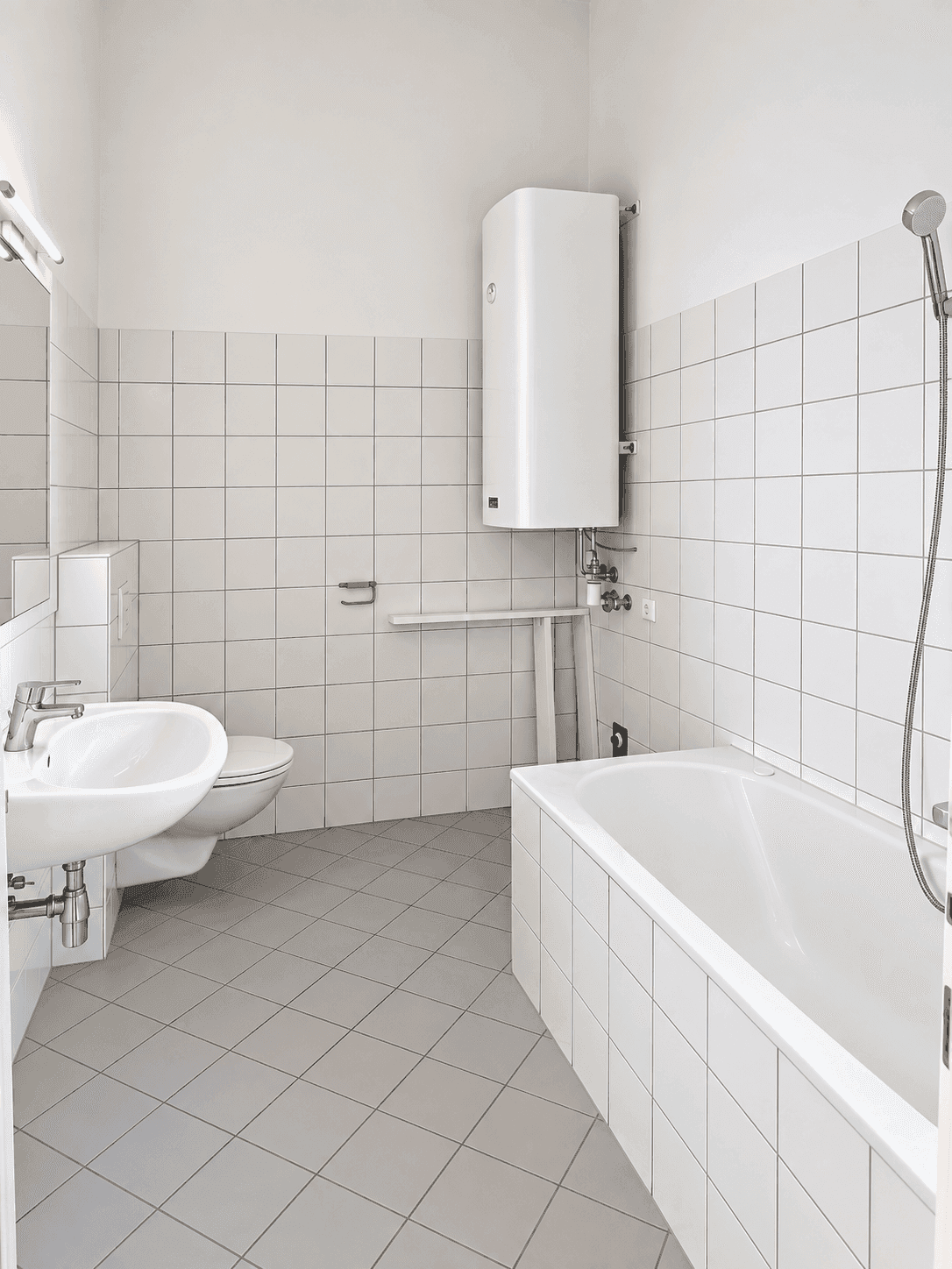 Helles Badezimmer mit Badewanne, WC, Waschbecken und einem Warmwasserboiler an der Wand.