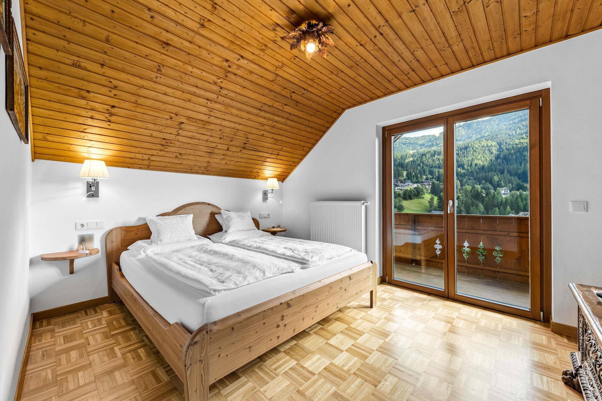Schlafzimmer mit Holzbett, Holzboden und Zugang zu einem Balkon mit Bergblick.
