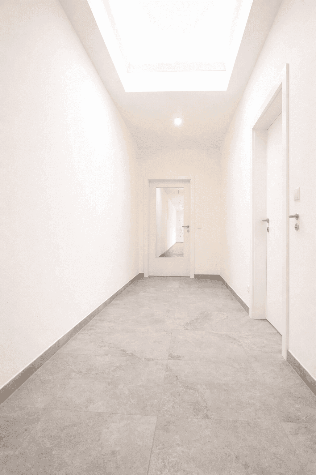 Heller Flur mit Fliesenboden und Oberlicht, der zu weiteren Räumen führt.