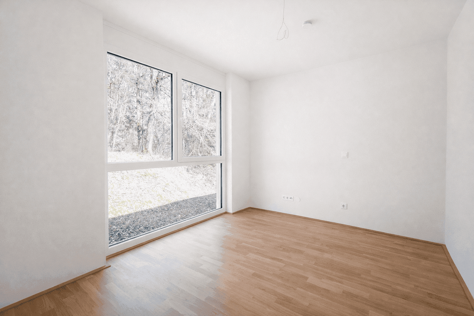 Helles Schlafzimmer mit Parkettboden und großem Fenster, das einen Blick ins Grüne bietet.